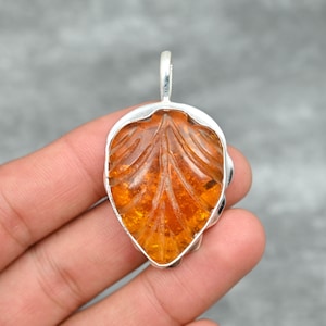 May include: A silver pendant featuring a carved amber leaf. The amber is a warm orange color and the pendant is detailed with intricate carvings.
