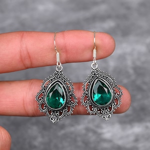 May include: A pair of silver dangle earrings with green gemstone drops. The earrings feature intricate filigree designs.