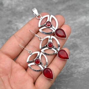 Pu&ograve; includere: Un set di ciondolo e orecchini in argento con accenti di pietre preziose rosse. Il ciondolo e gli orecchini presentano un design geometrico con una pietra rotonda centrale e una pietra a forma di lacrima.