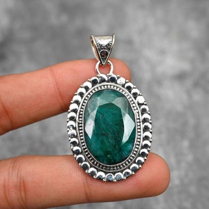May include: A silver pendant featuring a large, oval-shaped green gemstone set in a silver bezel. The bezel is decorated with a row of small silver beads.