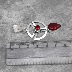 Pu&ograve; includere: Un ciondolo in argento con un design geometrico con due pietre preziose rosse. Il ciondolo misura circa 4 cm di lunghezza.