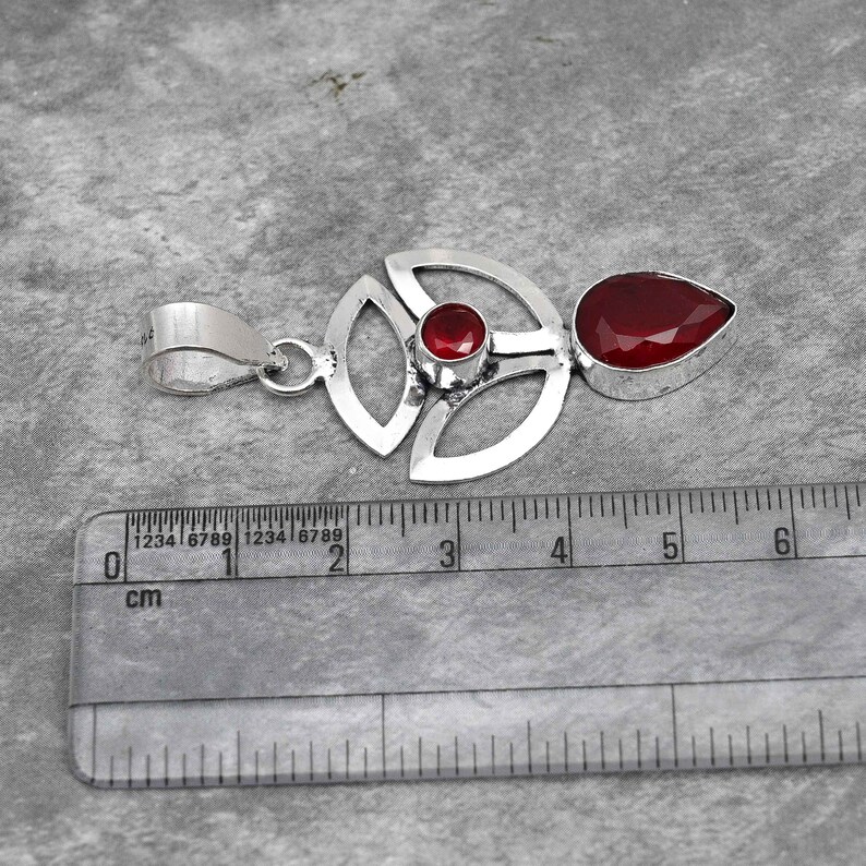 Pu&ograve; includere: Un ciondolo in argento con un design geometrico con due pietre preziose rosse. Il ciondolo misura circa 4 cm di lunghezza.