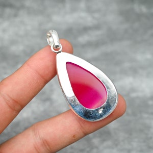 May include: A teardrop-shaped pendant with a vibrant pink stone set in a silver bezel. The polished stone has a smooth, glossy surface. The pendant has a silver loop at the top for a chain.