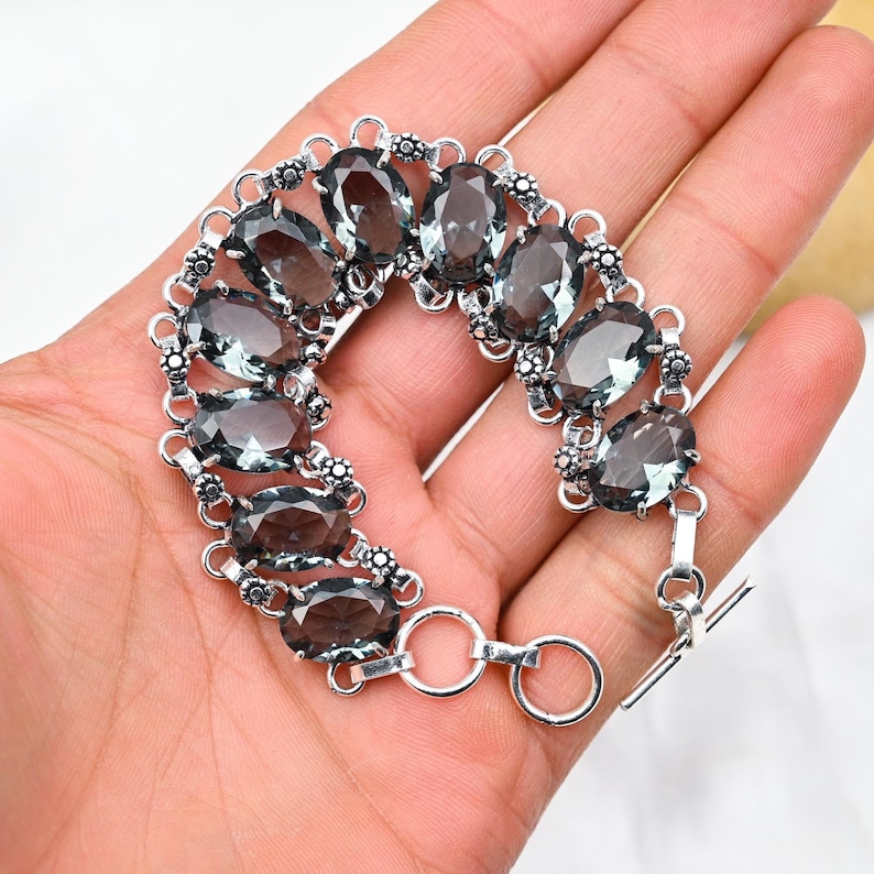 Puede incluir: Una pulsera de plata con una fila de piedras de cuarzo ahumado de forma ovalada. La pulsera tiene un cierre de barra en T.