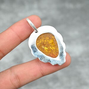 May include: Silver pendant with a teardrop-shaped amber stone set in a silver frame. The pendant has a scalloped edge and a bail for attaching a chain.