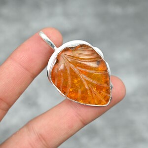 May include: A silver leaf pendant with a carved amber stone. The amber is a warm orange color and has a translucent quality.