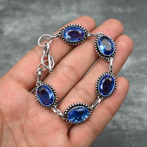 May include: A silver bracelet with five oval-shaped blue gemstones. The bracelet has a clasp closure.