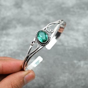 May include: A silver bangle bracelet with a green gemstone set in a decorative silver setting.