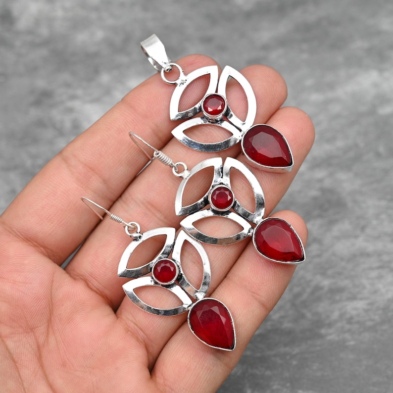 Pu&ograve; includere: Un set di ciondolo e orecchini in argento con accenti di pietre preziose rosse. Il ciondolo e gli orecchini presentano un design geometrico con una pietra rotonda centrale e una pietra a forma di lacrima.