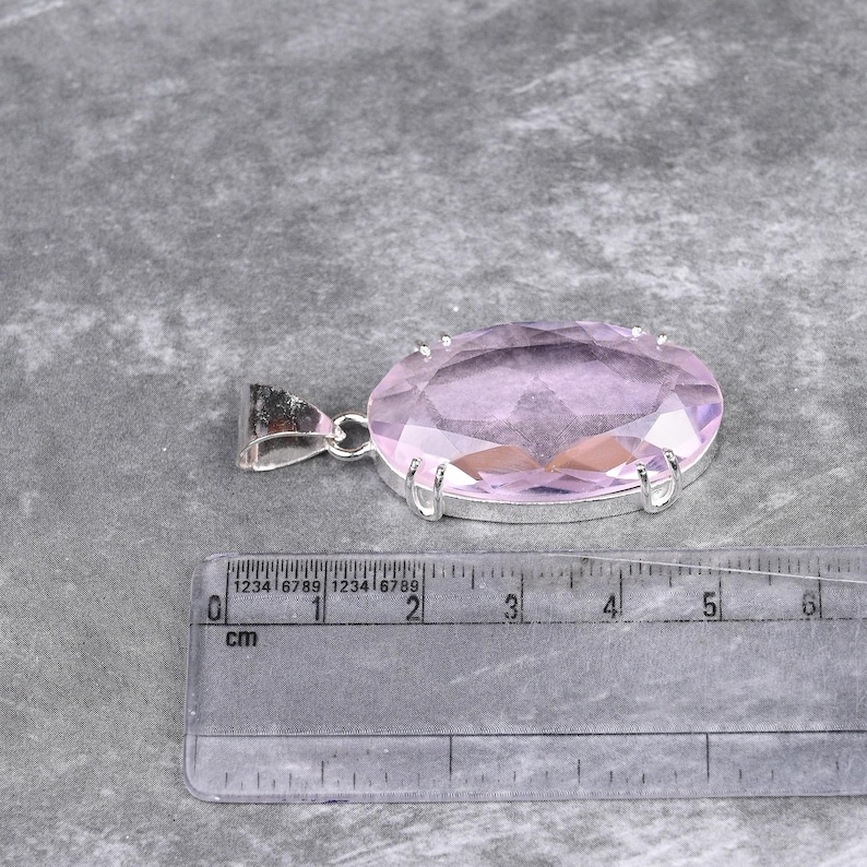 May include: A pale pink oval-shaped gemstone pendant with a silver setting. The pendant is approximately 2 cm in length.