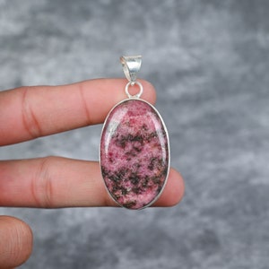 May include: A silver pendant featuring a pink and black oval-shaped rhodonite gemstone.