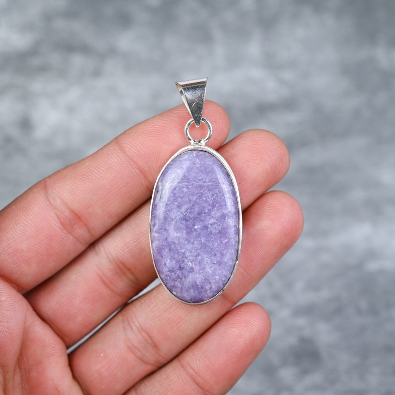 May include: A silver pendant featuring a light purple oval-shaped gemstone. The gemstone has a textured surface.