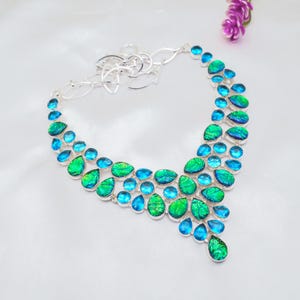 Peut inclure: Un collier en argent avec un design en cascade de pierres irisées bleues et vertes. Le collier est fait d'une chaîne en argent et présente une variété de pierres en forme de goutte.