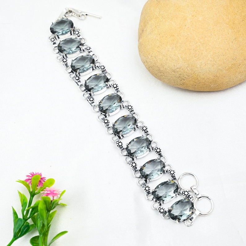 Puede incluir: Un brazalete de plata con un dise&ntilde;o de cadena de eslabones y piedras preciosas grises de forma ovalada. El brazalete tiene un cierre de langosta.