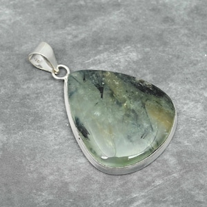 Peut inclure: Un pendentif en argent avec une pierre pr&eacute;cieuse verte et noire. La pierre pr&eacute;cieuse est en forme de larme et a une finition lisse et polie.