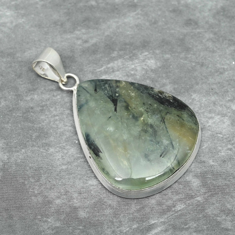 Peut inclure: Un pendentif en argent avec une pierre pr&eacute;cieuse verte et noire. La pierre pr&eacute;cieuse est en forme de larme et a une finition lisse et polie.