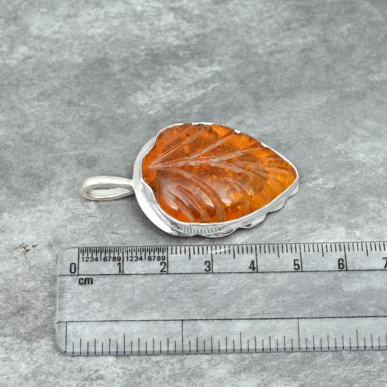 May include: A silver leaf pendant with a carved amber stone. The pendant is approximately 2 cm long.