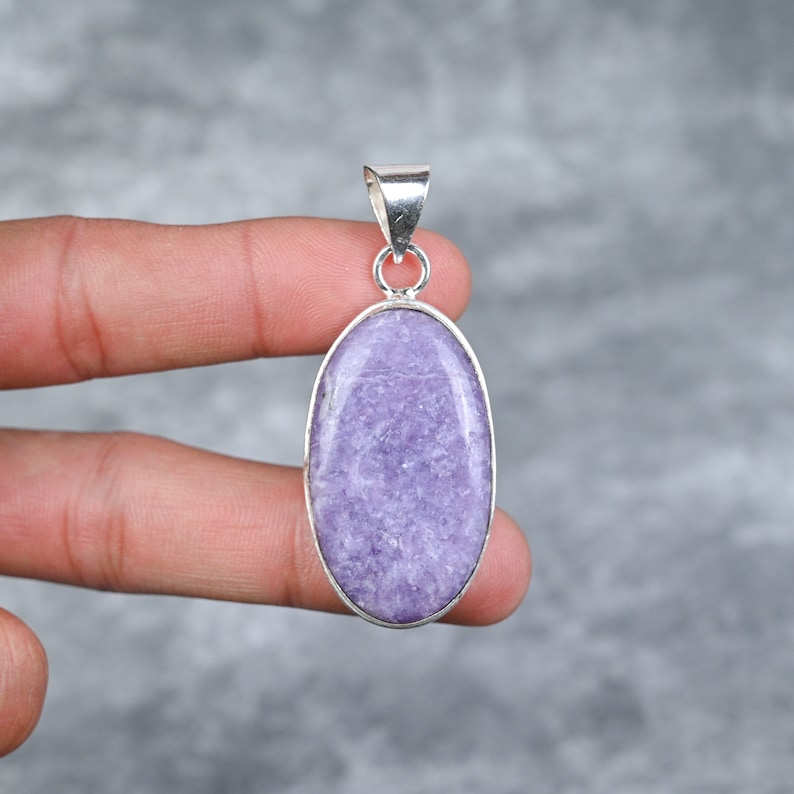 May include: A silver pendant featuring a large oval-shaped lavender lepidolite gemstone. The pendant has a simple design with a smooth, polished finish.