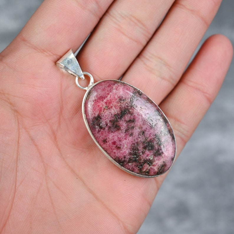 May include: A silver pendant featuring a pink and black oval-shaped gemstone. The pendant is on a silver chain.