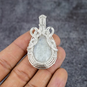 May include: A silver wire wrapped pendant featuring a white moonstone. The pendant has a teardrop shape and is accented with intricate wirework.