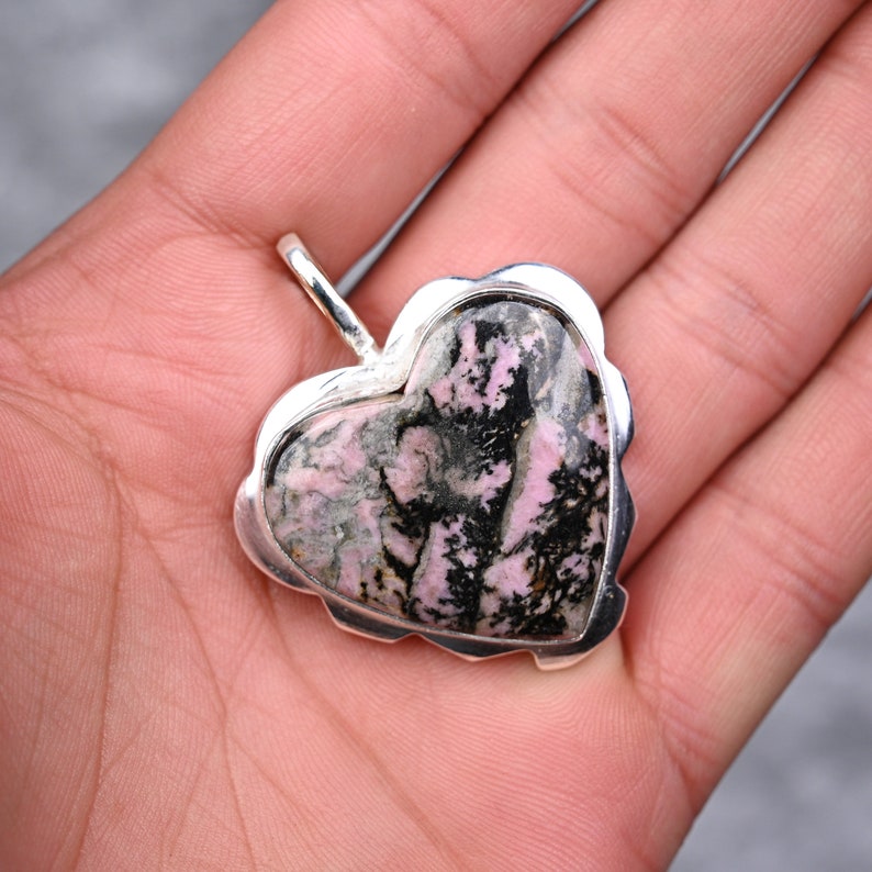 Op de afbeelding: Een hartvormige hanger met een zilveren frame. De hanger heeft een steen met roze, zwarte en grijze patronen. De hanger heeft een lus aan de bovenkant voor een ketting. De steen is gezet in een geschulpte zilveren rand.