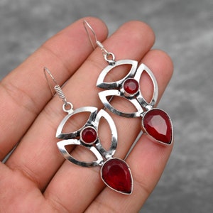 Pu&ograve; includere: Un paio di orecchini d'argento con un design geometrico e accenti di pietre preziose rosse. Gli orecchini presentano una pietra preziosa a forma di lacrima nella parte inferiore e una pietra preziosa rotonda pi&ugrave; piccola al centro.