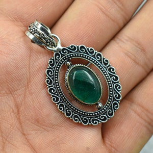 May include: A silver pendant with an oval, deep green gemstone set within a decorative, openwork frame. The frame features an ornate, swirling design and a detailed bail for a chain. The pendant is a piece of jewelry.