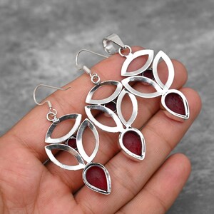 Pu&ograve; includere: Un set di ciondolo e orecchini in argento con un design di pietra preziosa rossa. Il ciondolo e gli orecchini presentano un motivo floreale con dettagli intricati.