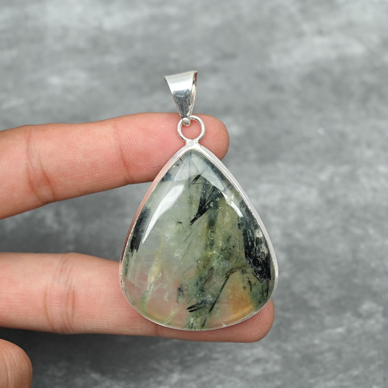 Peut inclure: Un pendentif en forme de larme avec une pierre pr&eacute;cieuse verte et noire transparente sertie dans de l'argent sterling.