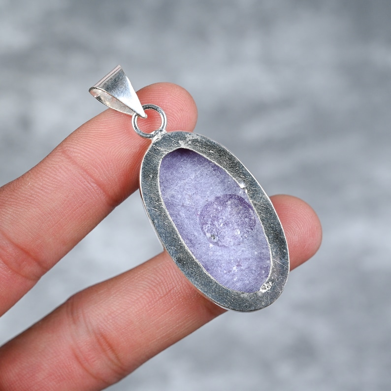 May include: A silver pendant featuring a purple amethyst crystal inside. The pendant is oval shaped and has a smooth, polished finish.