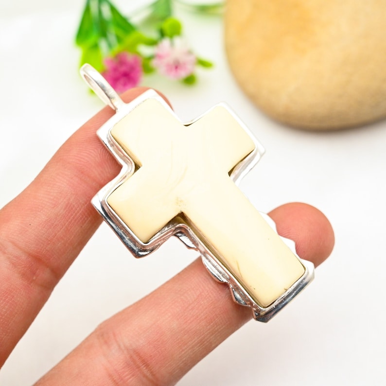 Peut inclure: Un pendentif en forme de croix blanche avec un cadre argent&eacute;. La croix est faite d'un mat&eacute;riau blanc lisse et a une surface l&eacute;g&egrave;rement textur&eacute;e. Le cadre argent&eacute; est orn&eacute; et pr&eacute;sente un design d&eacute;taill&eacute;.