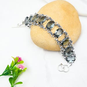 Puede incluir: Un brazalete de plata con un dise&ntilde;o de cadena de eslabones y piedras preciosas de cuarzo ahumado de forma ovalada. El brazalete tiene un cierre de palanca.