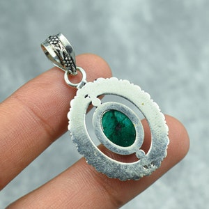 May include: A silver pendant with an oval, emerald-green stone set within an openwork design. The pendant has a decorative bail and a textured border. The metal is stamped with "925".