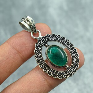 May include: A silver pendant with an oval, emerald-green gemstone set within a decorative, openwork frame. The frame has an ornate, swirling design and a bail for a chain.