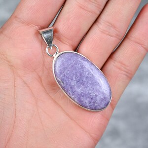 May include: A silver pendant featuring a large oval lavender gemstone. The pendant is displayed on a hand.
