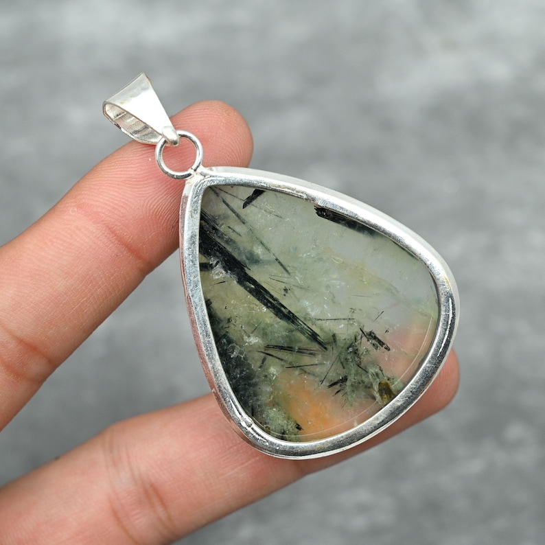 Peut inclure: Un pendentif en argent avec une pierre pr&eacute;cieuse verte et noire en forme de larme. La pierre pr&eacute;cieuse est sertie dans une b&eacute;li&egrave;re en argent.