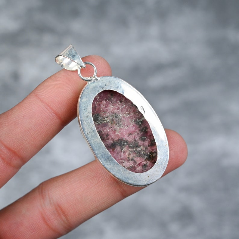 May include: A silver pendant with a pink and black rhodochrosite stone set in an oval bezel.