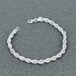 May include: A silver rope chain bracelet featuring a twisted metal design with a polished finish. The bracelet is constructed from interconnected silver links that form a continuous spiral pattern and includes a secure lobster claw clasp closure.