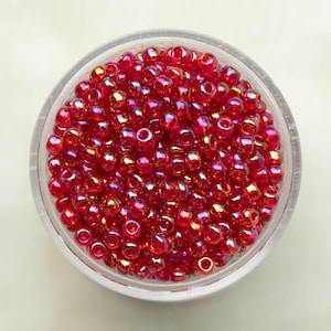 Puede incluir: Primer plano de un cuenco lleno de pequeñas cuentas rojas iridiscentes. Las cuentas tienen un brillo sutil y son perfectas para hacer joyas o manualidades.