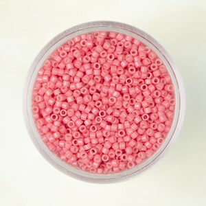 May include: A clear plastic container filled with small, pink, round beads.