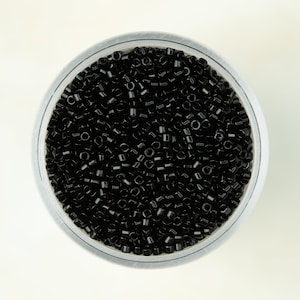 Peut inclure: Vue rapprochée d'un récipient transparent rempli de perles de rocaille noires.