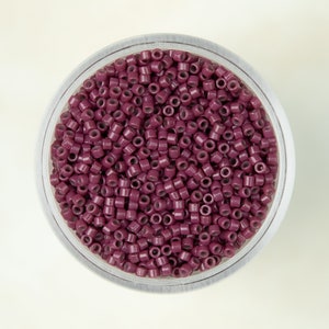 May include: A clear plastic container filled with small, round, dark purple beads.