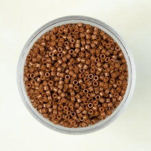 May include: A clear plastic container filled with small, brown, round beads.
