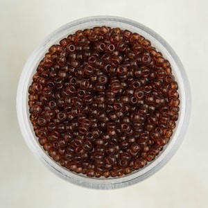Puede incluir: Un recipiente de plástico transparente lleno de pequeñas cuentas de vidrio redondas de color marrón.