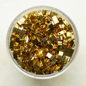 May include: A clear glass jar filled with a large quantity of gold-colored metal jump rings. The jump rings are small and have a rectangular shape.