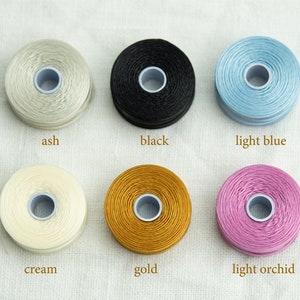 Peut inclure: Six bobines de fil &agrave; broder de diff&eacute;rentes couleurs&nbsp;: cendr&eacute;, noir, bleu clair, cr&egrave;me, or et orchid&eacute;e clair.