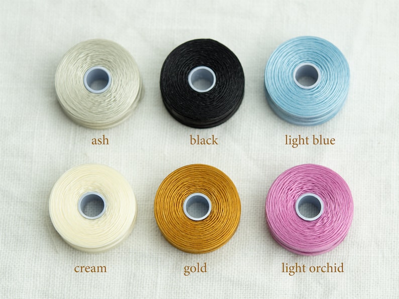 Peut inclure: Six bobines de fil &agrave; broder de diff&eacute;rentes couleurs&nbsp;: cendr&eacute;, noir, bleu clair, cr&egrave;me, or et orchid&eacute;e clair.