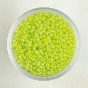 May include: A glass jar filled with small, light green glass beads. The beads have a slightly iridescent finish.
