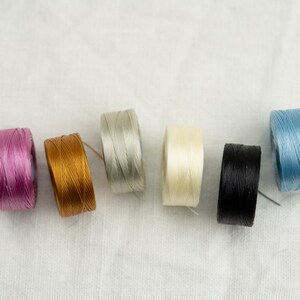 Peut inclure: Six bobines de fil de diff&eacute;rentes couleurs&nbsp;: rose, or, gris, blanc, noir et bleu.