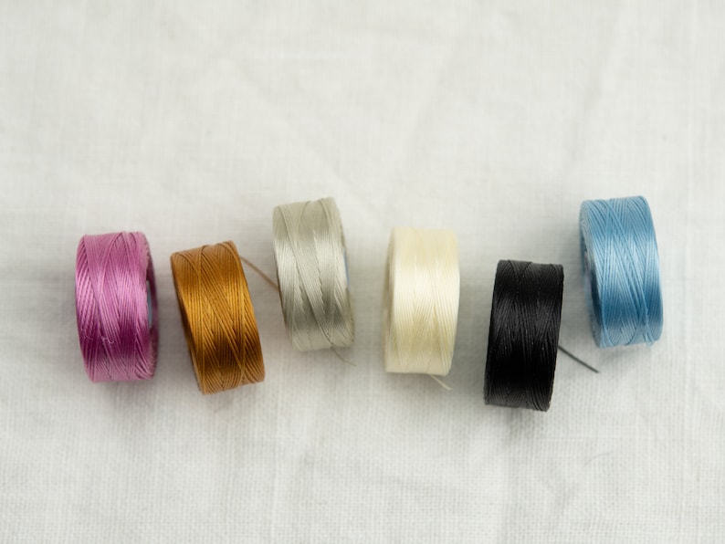 Peut inclure: Six bobines de fil de diff&eacute;rentes couleurs&nbsp;: rose, or, gris, blanc, noir et bleu.